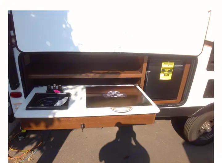 RV rental outdoor kitchen setup: A pull-out counter with a sink, covered cooktop, and mini-fridge, ideal for camping.. Forest River Tracer 2019