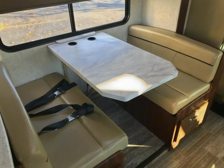 This RV rental dinette shows seating benches with seatbelts, a table with cupholders, and a view outside. Ideal for travel.. Forester 3271 LE 2018