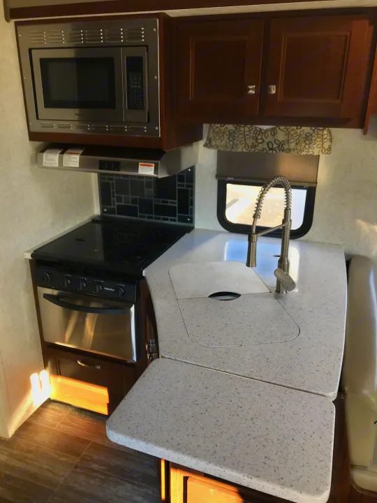 Inside an rv rental, this bright kitchen features a stainless microwave, oven/stove, and speckled countertops with a modern sink.. Forester 3271 LE 2018