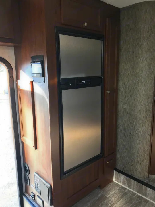 Inside an RV rental: view of kitchen area with stainless steel refrigerator, dark wood cabinets, and control panel.. Forester 3271 LE 2018
