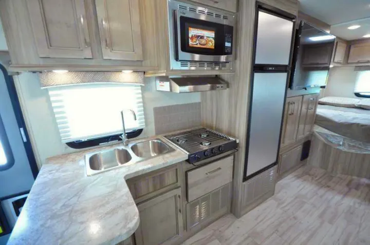 RV rental interior: functional kitchen with a double sink, three-burner stove, microwave, fridge, and adjacent bedroom.. Other Other 2019