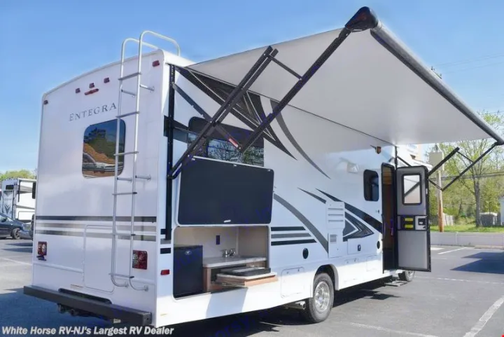 This white Entegra RV rental features a deployed awning, outdoor kitchen, TV, and rear ladder, ready for adventure.. Other Other 2019