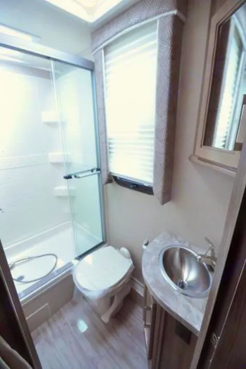This RV rental bathroom features a glass shower, toilet, and vanity with a stainless steel sink, maximizing space.. Other Other 2019