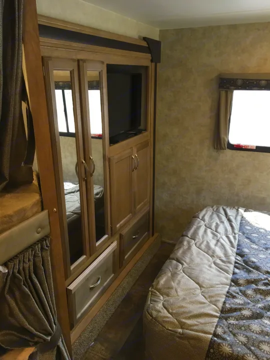 Cozy RV rental bedroom featuring a main bed, bunk, built-in TV, and mirrored storage.. Gulf Stream Conquest 2018