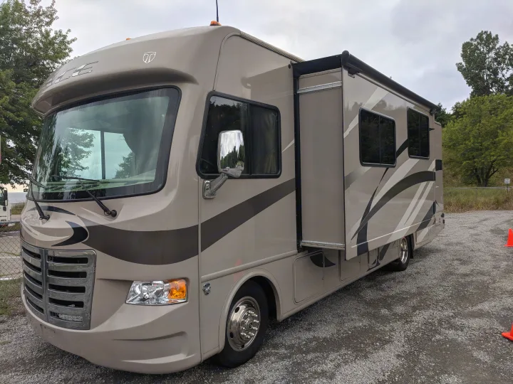 Light brown Class A motorhome for rv rental, featuring an extended slide-out on a gravel lot.. Thor Motor Coach A.C.E 2015