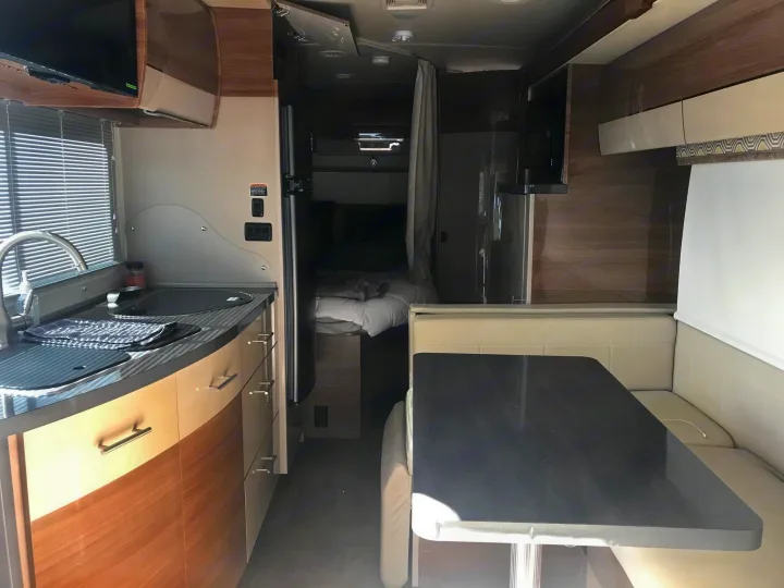 Inside a modern RV rental: kitchen, dining booth, and bedroom. An efficient, comfortable living space on the road.. Itasca Navion 2016