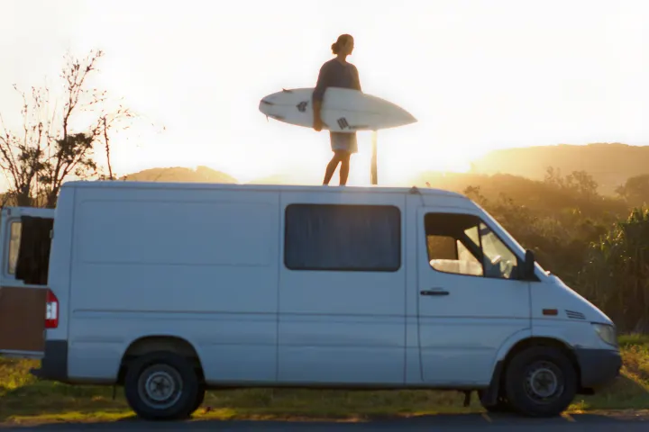 Surfer on an RV rental van with board at sunset, ready for van life adventures.. Mercedes-Benz Sprinter 2005