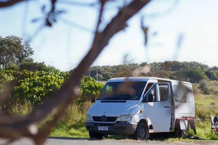White Mercedes-Benz Sprinter RV rental parked on a grassy verge with doors open, wetsuit on a stand, hinting at outdoor adventure.. Mercedes-Benz Sprinter 2005