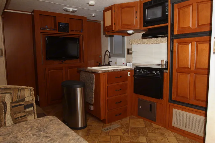 Explore this RV rental's well-equipped kitchen with a sink, stove, microwave, and refrigerator, plus a TV and seating.. Forest River Surveyor 2010