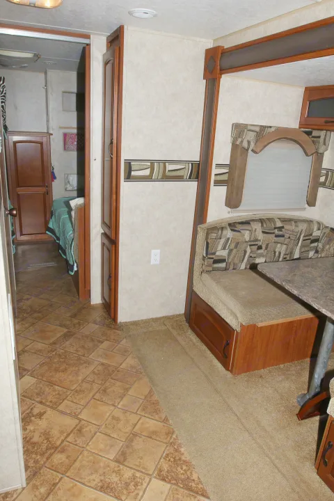 RV rental interior showcasing a cozy dinette with patterned cushions, a tiled entryway transitioning to carpet, and a bedroom beyond.. Forest River Surveyor 2010