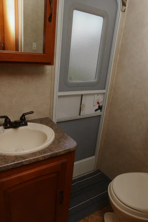 This RV rental features a compact bathroom with a sink, dark vanity, toilet, and an interior door with a frosted window.. Forest River Surveyor 2010