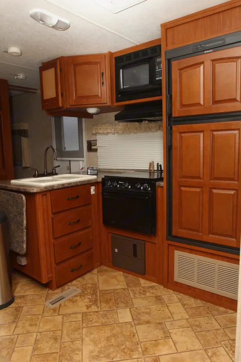 Compact RV rental kitchen with wood cabinets, sink, oven, microwave, fridge, and tile floor.. Forest River Surveyor 2010