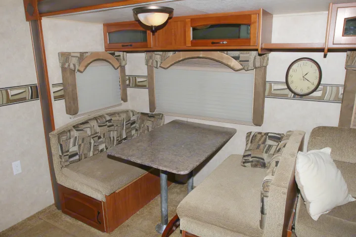 RV rental interior: A comfortable dining booth with upholstered seats, a table, overhead cabinets, and windows with blinds.. Forest River Surveyor 2010
