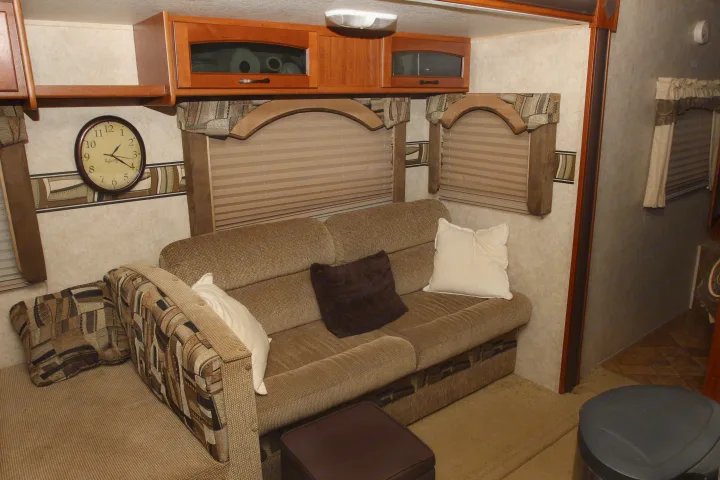 Cozy RV rental interior with a comfortable sofa, decorative pillows, wall clock, and overhead cabinets.. Forest River Surveyor 2010