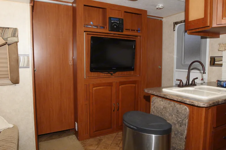RV rental interior: living area with entertainment center, TV, and kitchen counter with sink, flanked by sliding doors.. Forest River Surveyor 2010