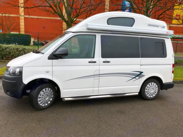 White campervan RV rental, parked on asphalt. Features a high roof and side steps, ideal for travel.. Volkswagen T5 Vivante 2015