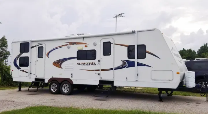 This large white travel trailer, a Surveyor Eco-Lite, is parked and set up, ready for your next RV rental adventure.. Forest River Surveyor 2010