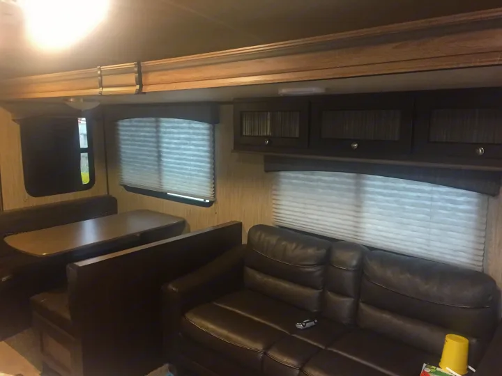 Inside this RV rental: a bright living area with a dinette, plush sofa, windows, and overhead cabinets.. Heartland Sundance 2018