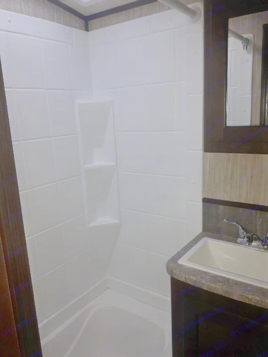 Compact RV rental bathroom featuring a white tiled shower/tub, built-in shelves, shower rod, dark vanity, sink, and mirror.. Heartland Sundance 2018