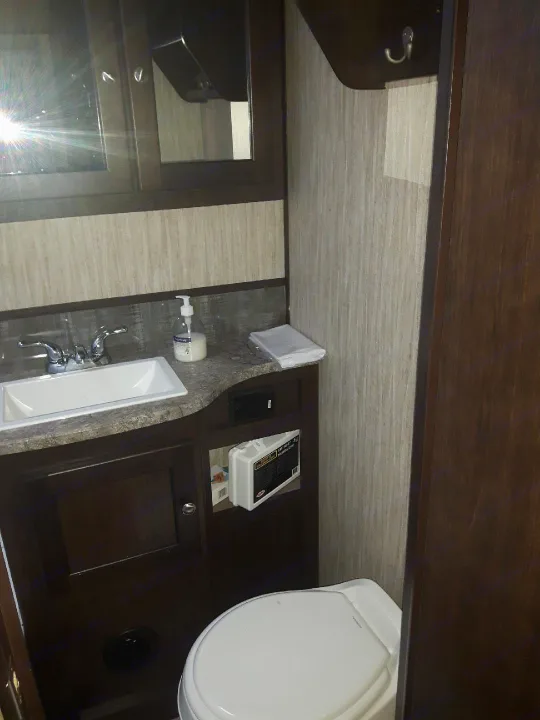 RV rental bathroom features a compact sink, toilet, mirrored cabinet, and first aid kit on a dark wood vanity.. Heartland Sundance 2018