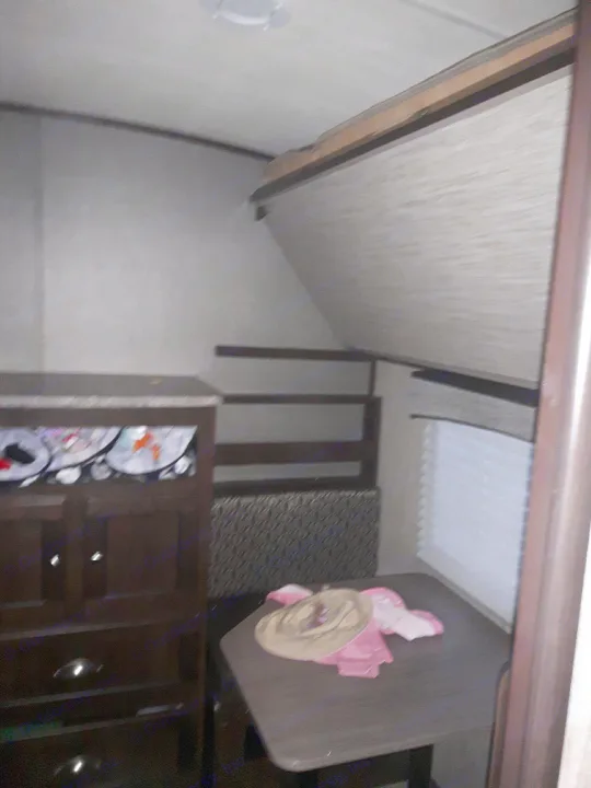 Compact rv rental interior shows a dinette with a hat, window blinds, bunk beds, and a dresser for practical living space.. Heartland Sundance 2018