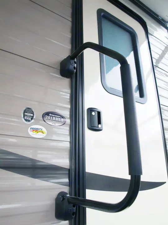 This RV rental's exterior features a light-colored door with a black grab handle, ensuring safe entry into the travel trailer.. K-Z Manufacturing Sportsmen LE 261BHLE 2019
