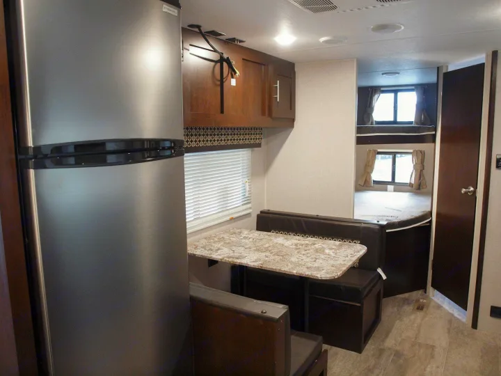 An RV rental interior with a dinette, stainless steel fridge, and bunk beds, ideal for family trips.. K-Z Manufacturing Sportsmen LE 261BHLE 2019