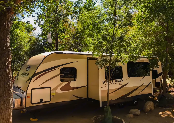 A large Jayco White Hawk RV rental, with a slide-out extended, is parked in a tree-shaded campsite.. Jayco White Hawk Ultra Lite 2015