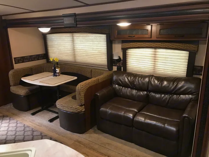 Cozy RV rental interior features a U-shaped dinette with flowers, a table, and a plush leather sofa, perfect for relaxing travel.. Jayco White Hawk Ultra Lite 2015