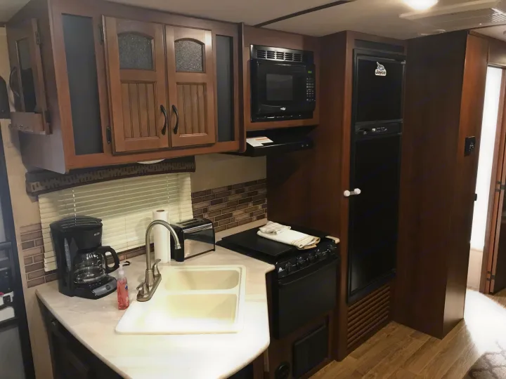 This RV rental kitchen boasts wooden cabinets, a microwave, stove, fridge, sink, coffee maker, and toaster for convenient travel.. Jayco White Hawk Ultra Lite 2015