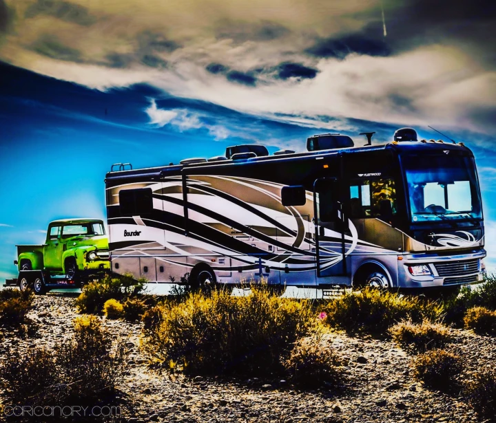 RV rental trip: A large Fleetwood Bounder motorhome parked in the desert, towing a vintage green pickup truck on a flatbed.. Fleetwood Bounder 2015