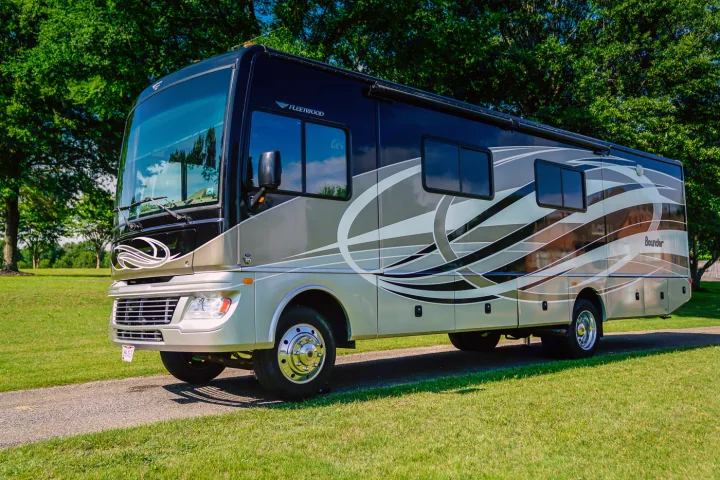 A sleek Fleetwood Bounder Class A RV rental, black and tan with gray swirls, parked on a gravel path amidst green grass.. Fleetwood Bounder 2015