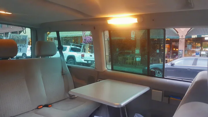 View from an RV rental: comfy interior with a table and a rainy town street outside.. Volkswagen Eurovan 1999