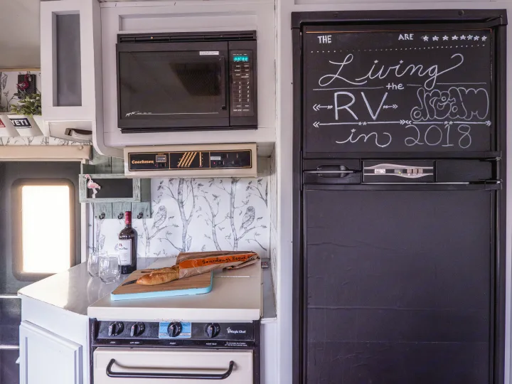 An RV rental kitchen with microwave, stove, and fridge, showcasing personal touches and the "Living the RV Dream" message.. Other Other 1992