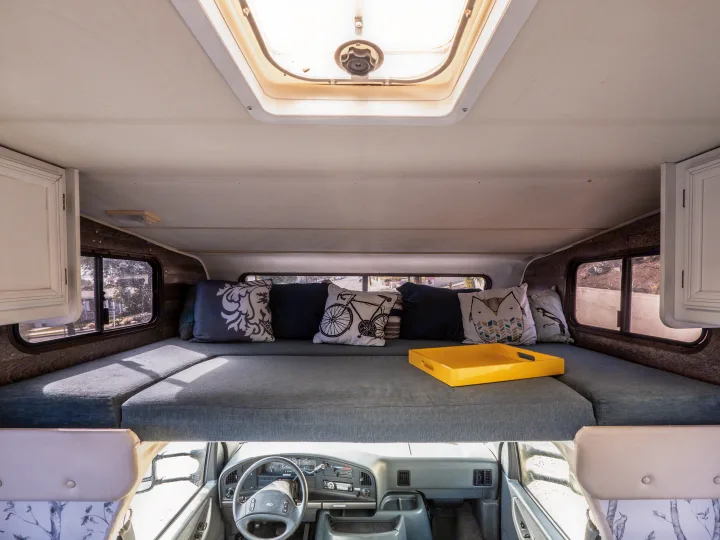 Spacious RV rental interior: overhead bed with pillows, bright skylight, and cockpit view. Ideal camper living space.. Other Other 1992