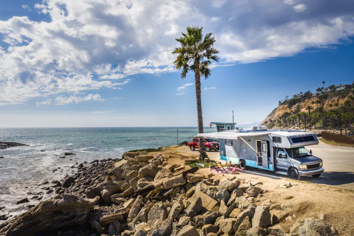 RV rental parked on a scenic coastal spot with a palm tree, rocky beach, and ocean views.. Other Other 1992