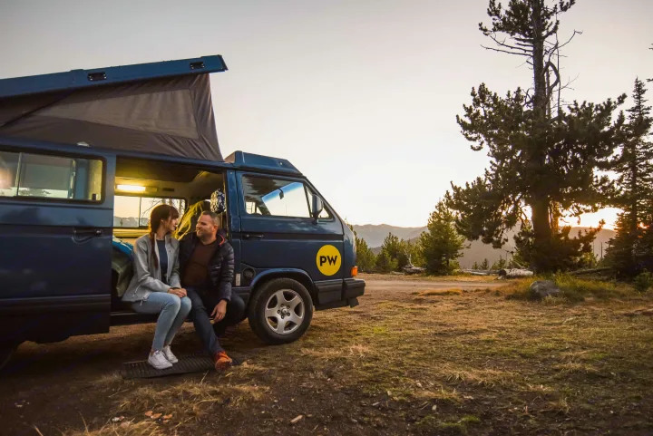 Couple enjoys their RV rental trip, relaxing in a pop-top campervan with mountain sunset views.. Volkswagen Westfalia 1991