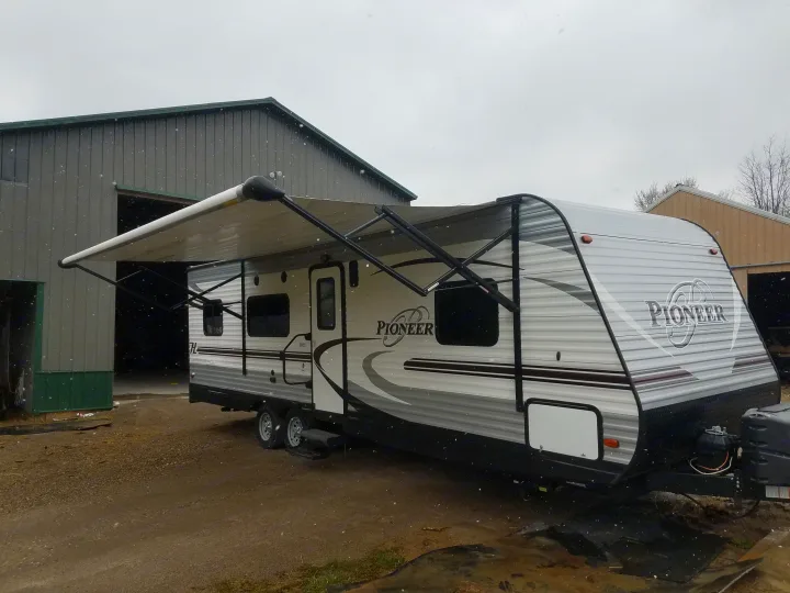 Pioneer RV rental travel trailer with extended awning, parked outside a building during light snowfall.. Heartland Pioneer 2016