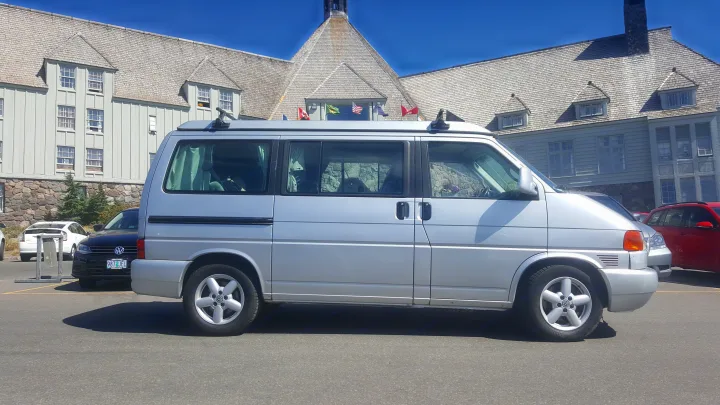 Silver VW pop-top camper van, an ideal rv rental, parked by a large, light-colored lodge on a sunny day.. Volkswagen Westfalia 2002