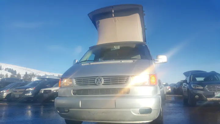 Front view of a silver VW camper van with its pop-top open, parked in a snowy mountain lot. Great rv rental for winter trips!. Volkswagen Westfalia 2002