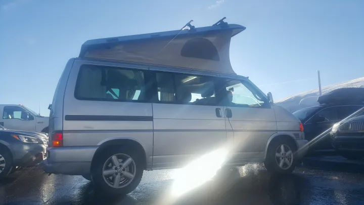 Silver VW pop-top camper van (RV rental) shines in the sun, parked on a wet lot near snow. Ready for travel.. Volkswagen Westfalia 2002