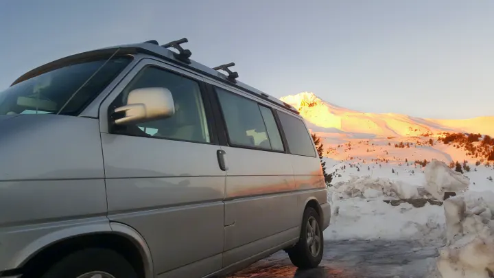 Silver RV rental van parked in a scenic snowy mountain landscape at sunrise, with a prominent peak illuminated in the background.. Volkswagen Westfalia 2002