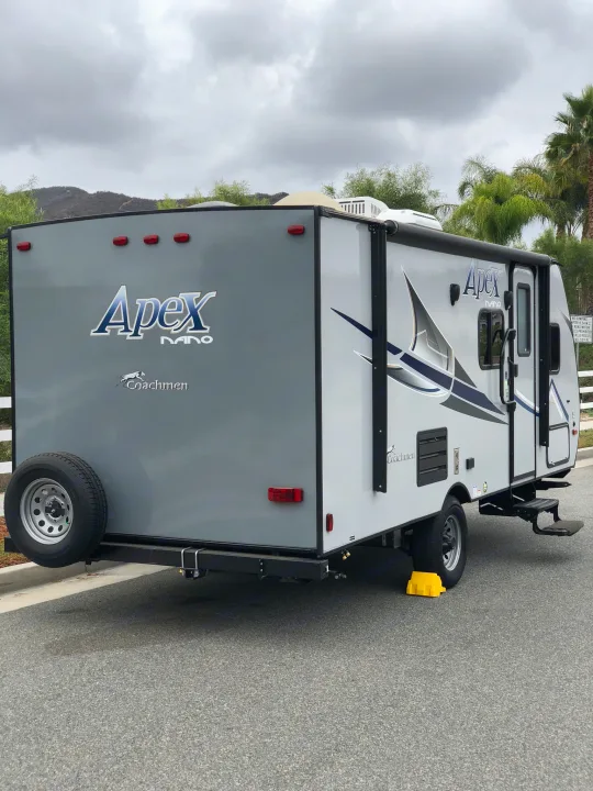 This Apex Nano travel trailer is ready for your next RV rental adventure, parked on asphalt with leveling blocks.. Coachmen Apex 2018