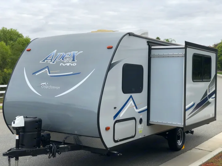 This modern grey Apex Nano travel trailer with an open slide-out is perfect for an RV rental, parked outdoors.. Coachmen Apex 2018