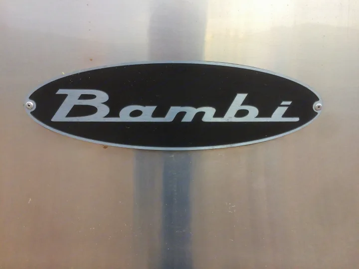 Close-up of a silver metallic "Bambi" logo on a black oval plaque, attached to a shiny RV surface. Ideal for an RV rental.. Airstream Sport 2012