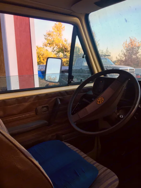 Driver's view from an RV rental, featuring steering wheel, dashboard, and autumn outdoor scenery including a barn.. Volkswagen Vanagon 1984