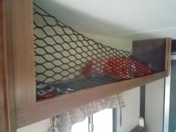 An RV rental features practical overhead storage netting, keeping personal items like a red blanket secure during travel.. Heartland Pioneer 2016
