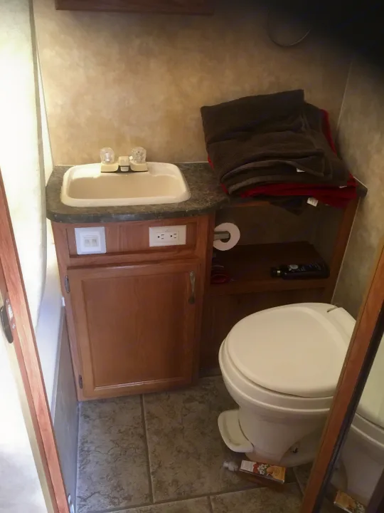 Compact RV rental bathroom features a sink, toilet, cabinet, and storage for towels, ideal for travel.. Jayco Jay Feather Ultra Lite 2012