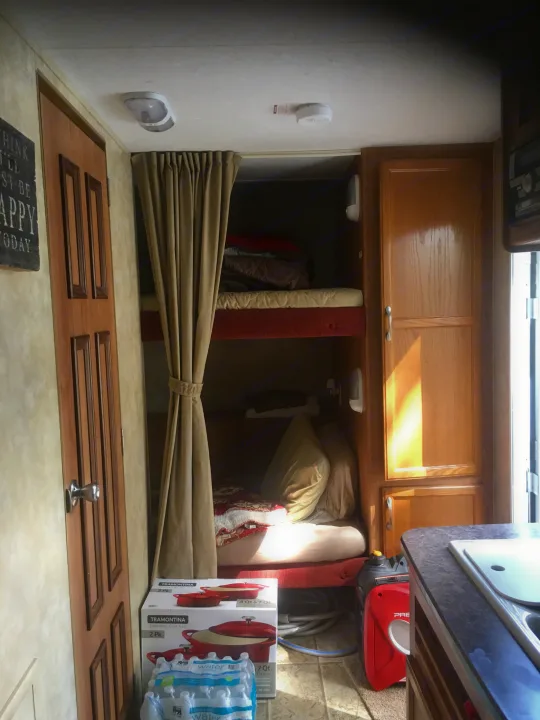 Inside an RV rental, featuring bunk beds with privacy curtains, a compact kitchenette, and storage. Ideal for family travel.. Jayco Jay Feather Ultra Lite 2012