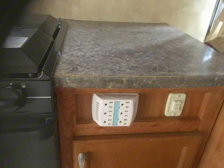 RV rental kitchen: Countertop, stove, multi-plug, and control switch on wood cabinets.. Jayco Jay Feather Ultra Lite 2012